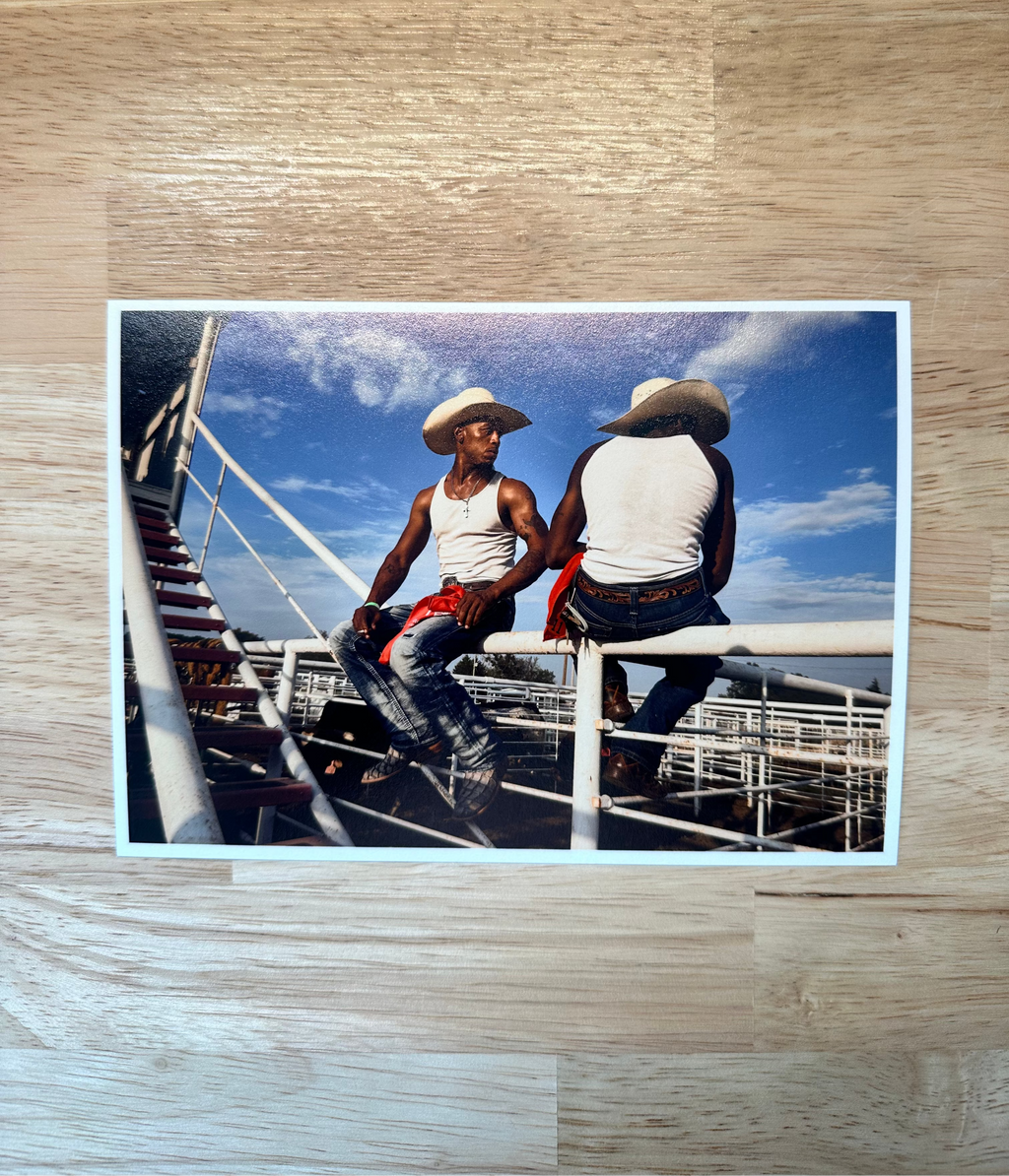 Two people sitting on a fence with a scenic background, placed on a wooden surface.